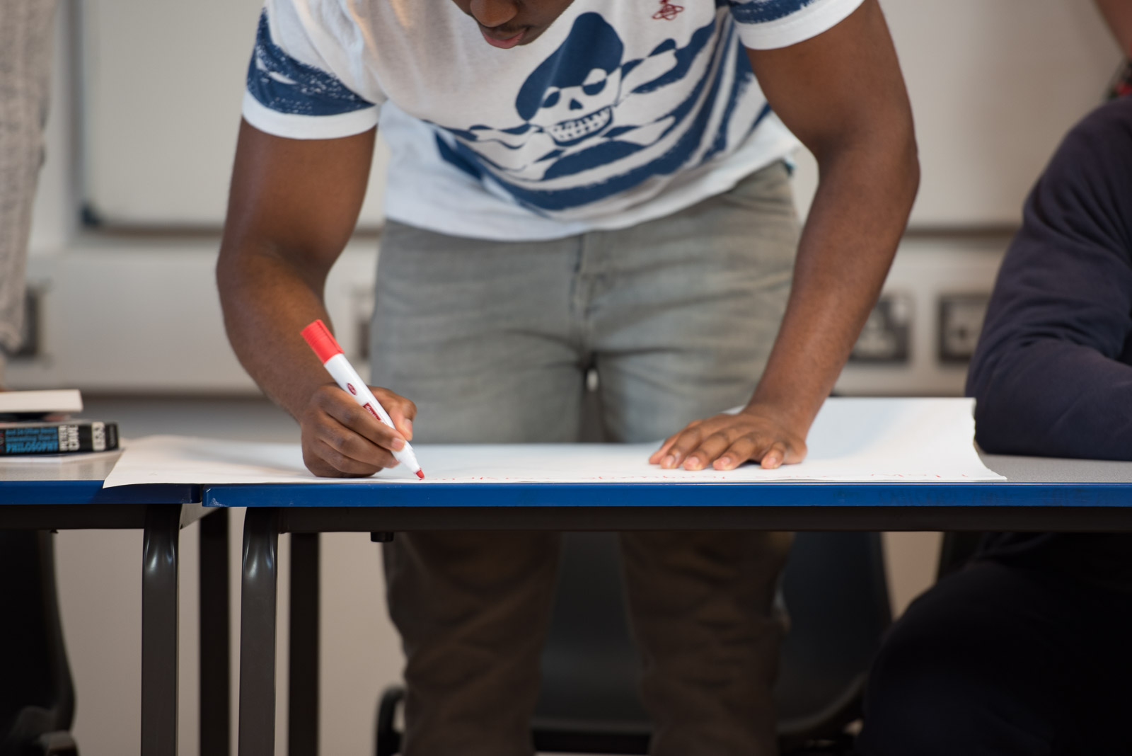 Learner standing up and writing on paper on desk